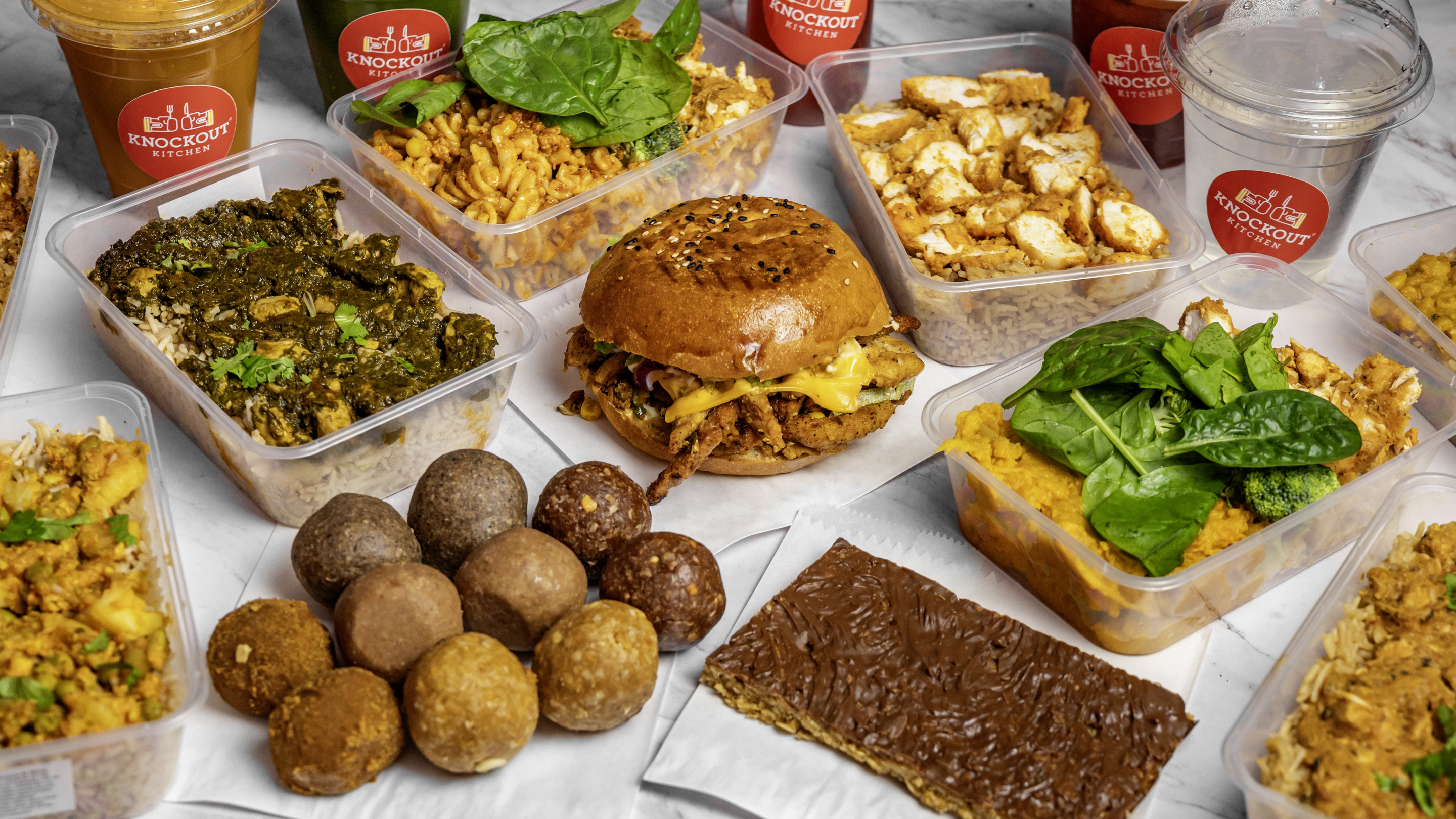 Spread of Knockout Kitchen meal prep boxes, burger, juices, protein balls and snacks